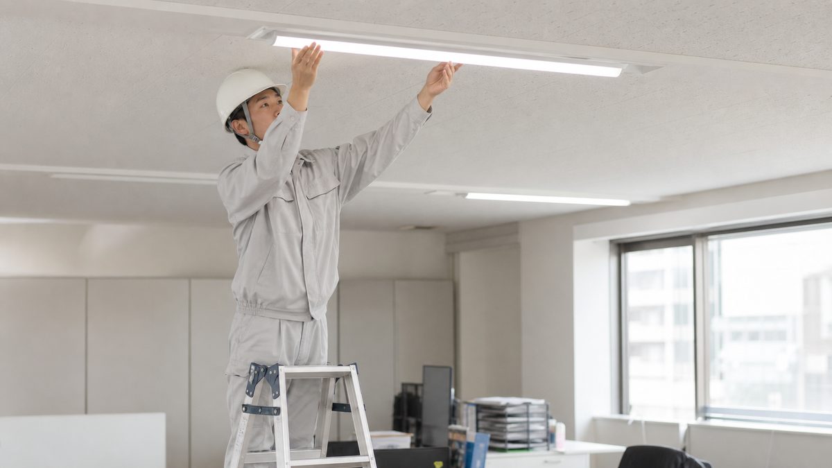 脚立に乗って天井の照明器具を交換する作業者